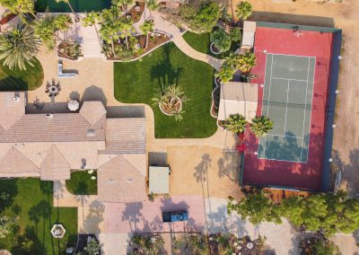 A bird's-eye-view of the Estate House at Rancho de las Palmas. Visible are the house itself, a tennis court, a small yard, and a private lagoon