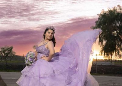 a woman in a purple wedding dress poses in front of a sunset