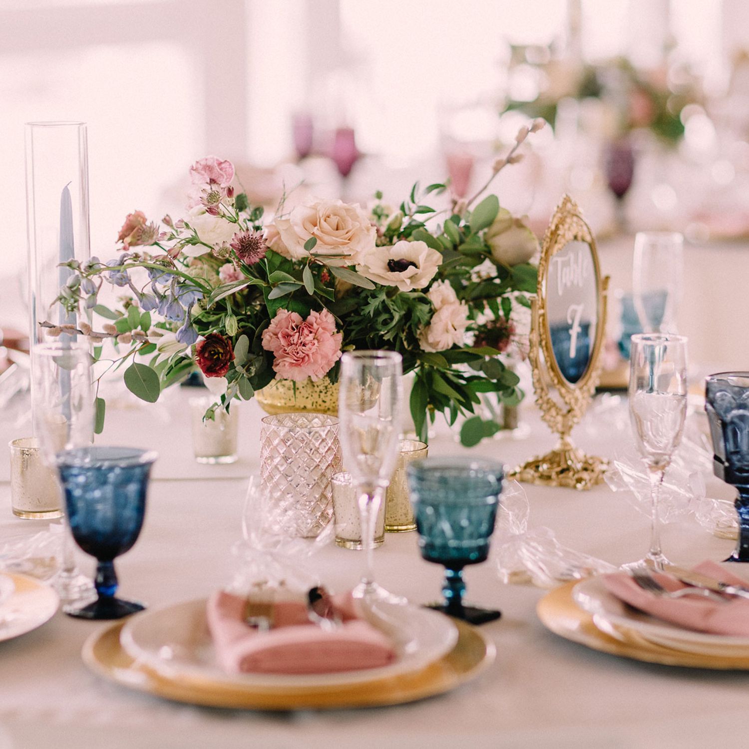 a vase of flowers, champagne glasses, silverware, and plates nicely arranged on a wedding reception table