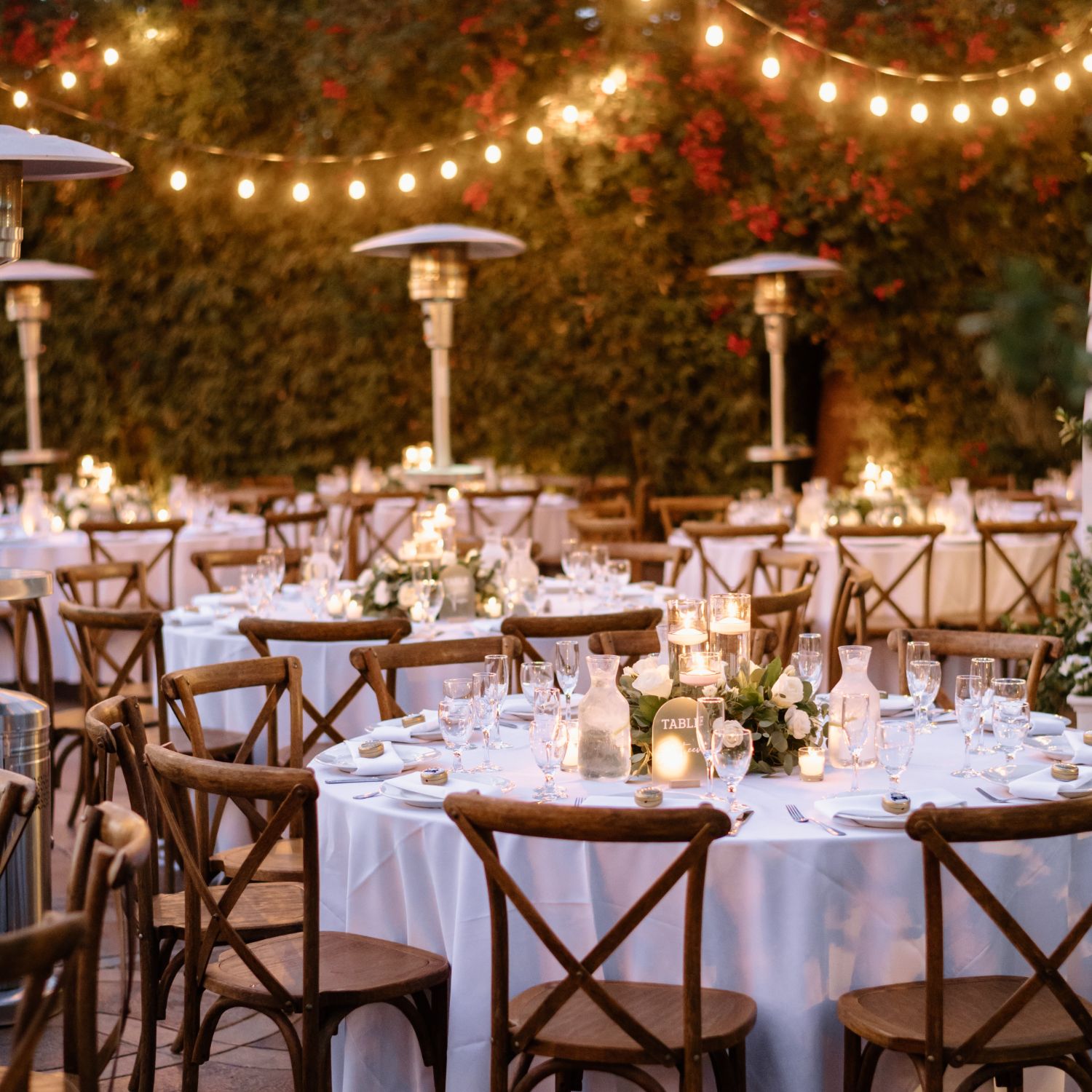 An outdoor wedding reception area with round, white tables and hanging lights